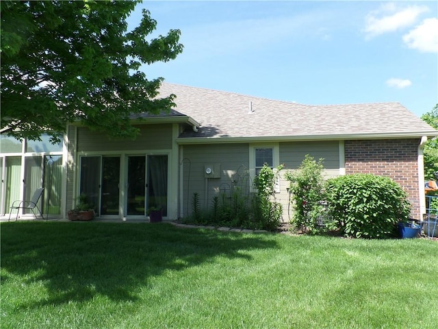 rear view of property featuring a lawn, a shingled roof, and brick siding