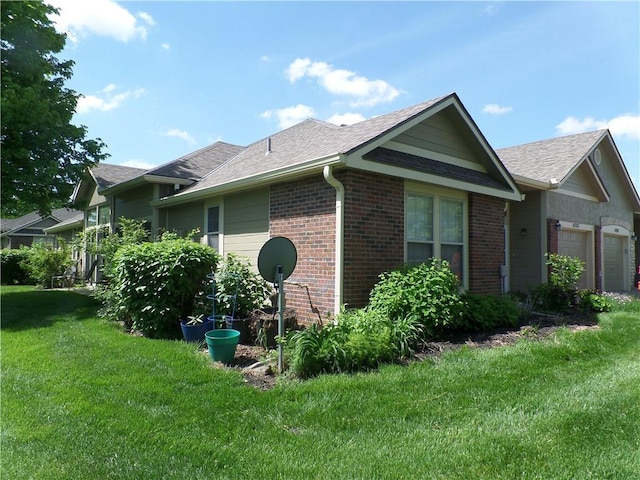 view of side of property with a lawn, a garage, roof with shingles, and brick siding
