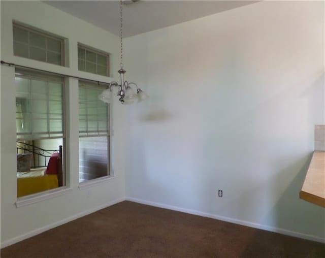 unfurnished dining area with an inviting chandelier, baseboards, and dark colored carpet