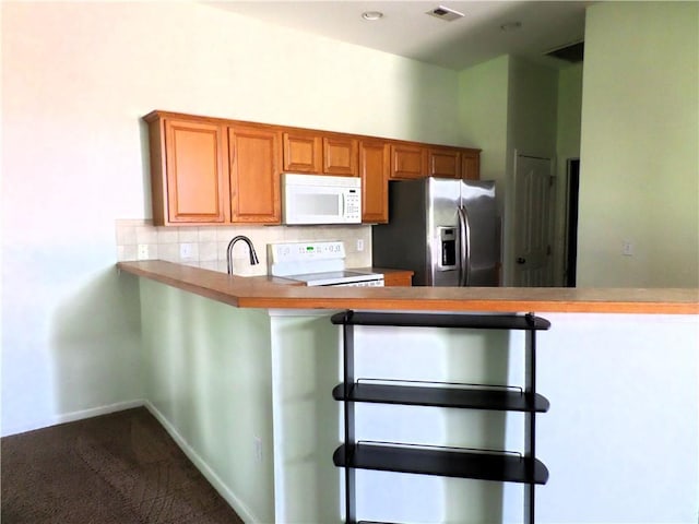 kitchen featuring visible vents, a peninsula, white appliances, dark colored carpet, and tasteful backsplash