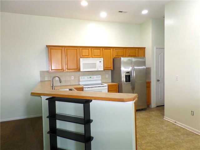 kitchen featuring a peninsula, white appliances, light countertops, tasteful backsplash, and a sink