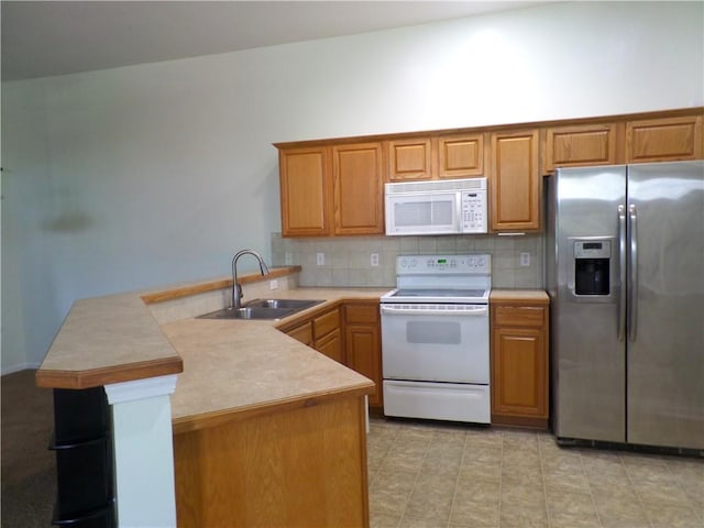 kitchen featuring a sink, tasteful backsplash, a peninsula, and white appliances