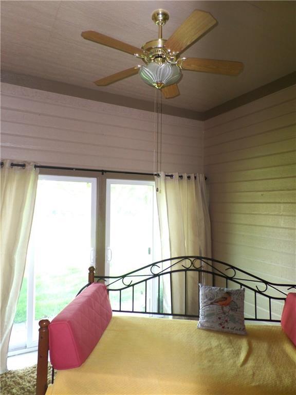 bedroom featuring carpet floors, ceiling fan, wooden walls, and multiple windows