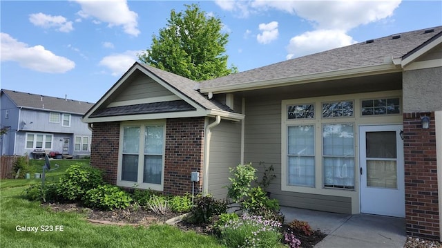 view of home's exterior with roof with shingles, a patio area, and brick siding