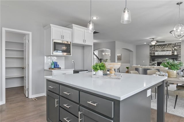 kitchen with stainless steel microwave, white cabinets, arched walkways, ceiling fan with notable chandelier, and hanging light fixtures