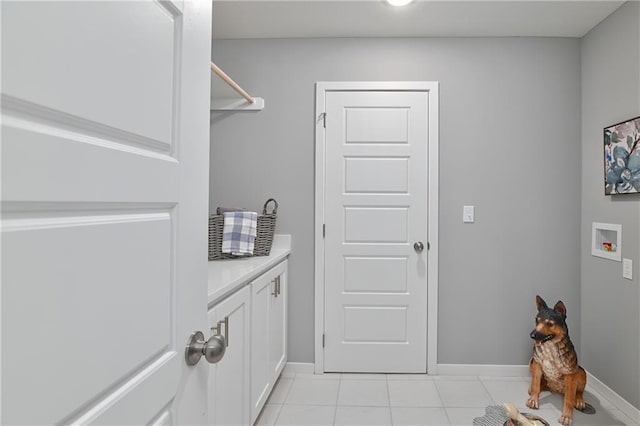 clothes washing area with light tile patterned floors, washer hookup, baseboards, and cabinet space