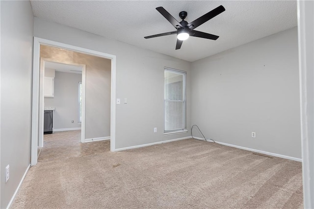 spare room featuring light carpet, a ceiling fan, baseboards, and a textured ceiling