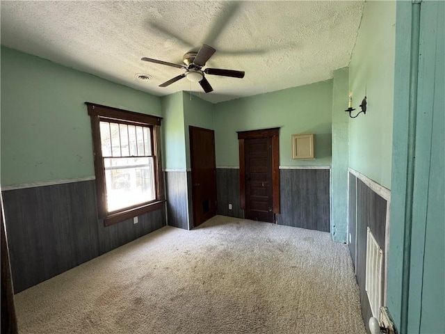 318 S Williams St, Craig, MO 64437 - unfurnished bedroom featuring wooden walls, wainscoting, light carpet, a textured ceiling, and visible vents