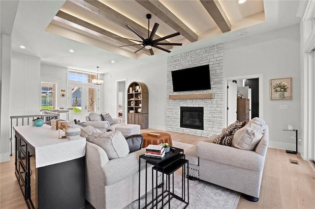 living room featuring ceiling fan, a stone fireplace, beamed ceiling, light wood finished floors, and recessed lighting
