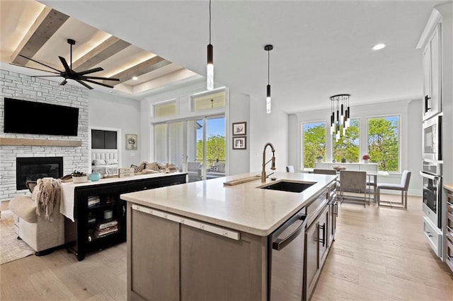 kitchen featuring stainless steel appliances, a sink, light wood-style floors, a center island with sink, and open floor plan