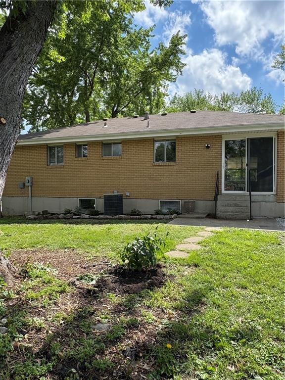 rear view of house with a lawn, central AC, and brick siding