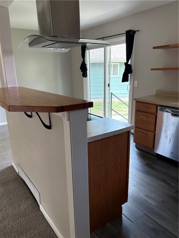 kitchen featuring stainless steel dishwasher, open shelves, butcher block countertops, island range hood, and a kitchen bar