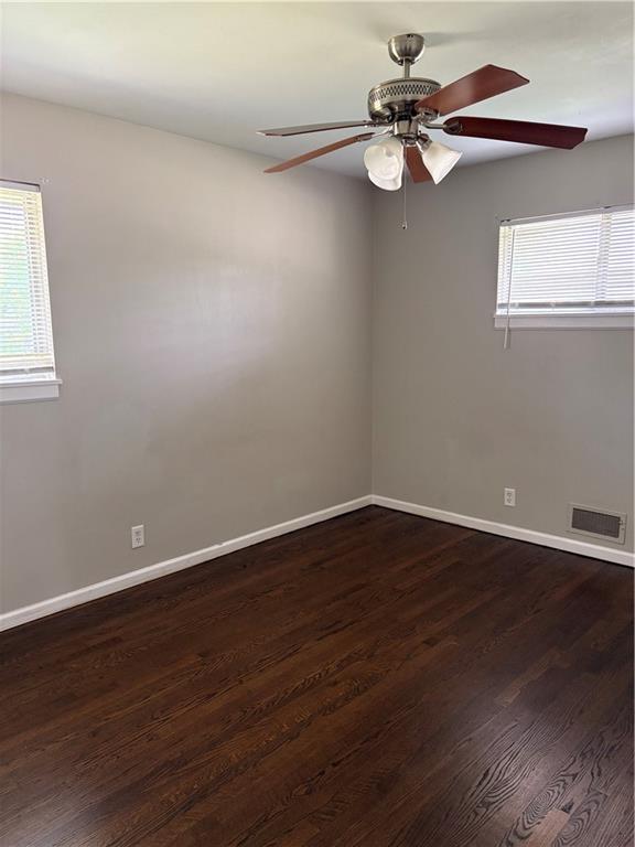 empty room with a ceiling fan, baseboards, visible vents, and dark wood-type flooring