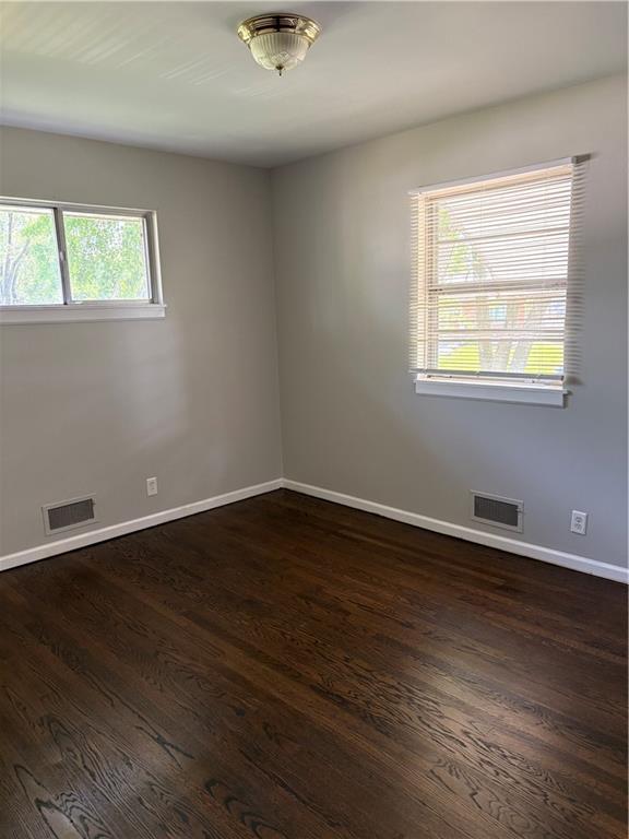 empty room featuring visible vents, dark wood finished floors, and baseboards