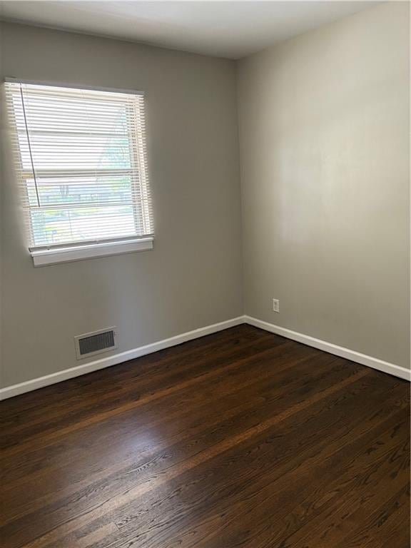 unfurnished room featuring baseboards, dark wood-type flooring, and visible vents