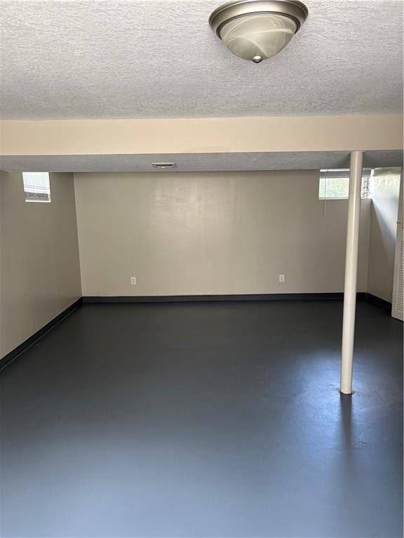 basement featuring baseboards, a textured ceiling, and a healthy amount of sunlight