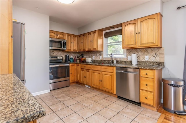 kitchen featuring dark stone counters, a sink, appliances with stainless steel finishes, and backsplash
