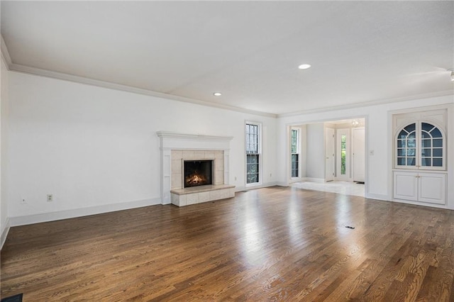 unfurnished living room with ornamental molding, wood finished floors, baseboards, a tiled fireplace, and recessed lighting