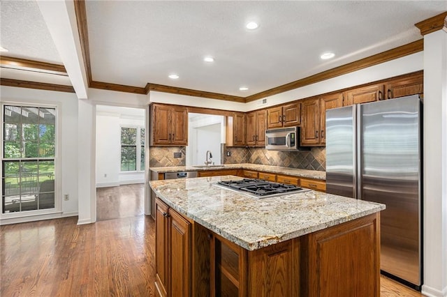 kitchen featuring stainless steel appliances, ornamental molding, light wood-style flooring, a center island, and decorative backsplash