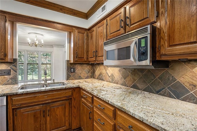 kitchen featuring stainless steel appliances, backsplash, a chandelier, brown cabinets, and ornamental molding