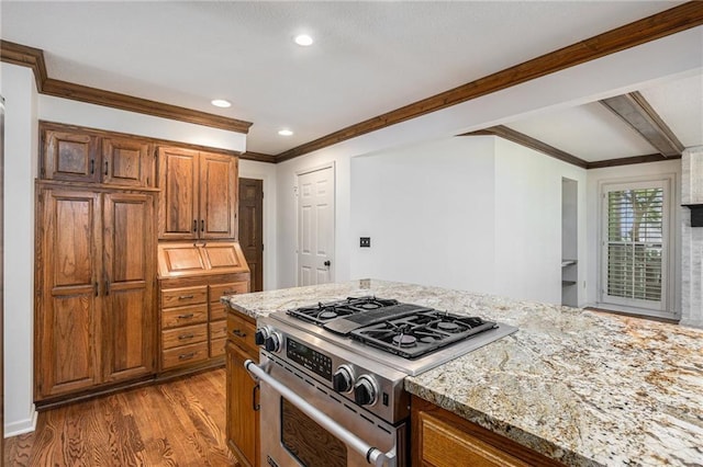 kitchen featuring stainless steel range with gas stovetop, ornamental molding, light wood finished floors, light stone counters, and recessed lighting