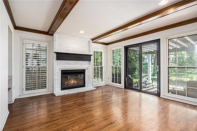 unfurnished living room with beamed ceiling, ornamental molding, wood finished floors, a brick fireplace, and a textured ceiling