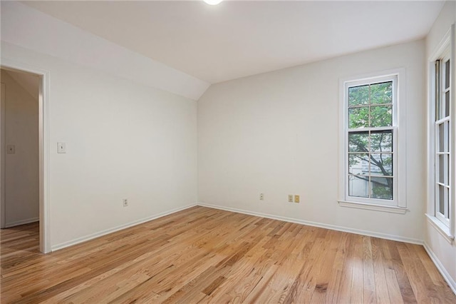empty room featuring light wood-type flooring, baseboards, and vaulted ceiling