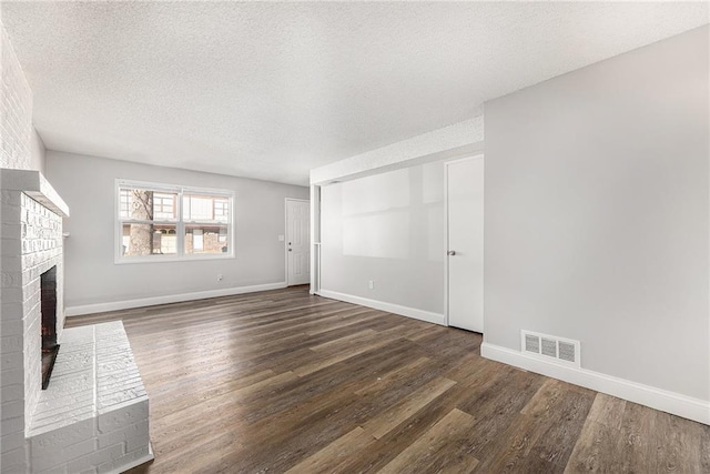unfurnished living room featuring visible vents, a textured ceiling, a brick fireplace, and wood finished floors