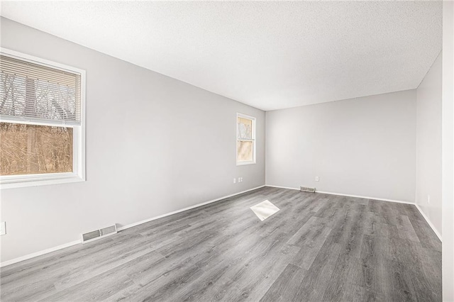 empty room featuring a wealth of natural light, wood finished floors, and visible vents