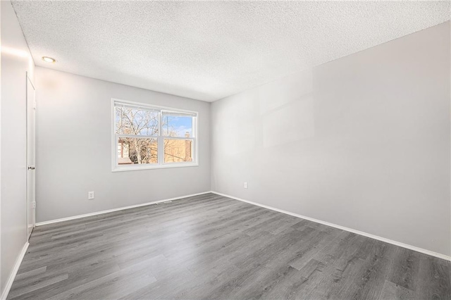 empty room with a textured ceiling, baseboards, and wood finished floors