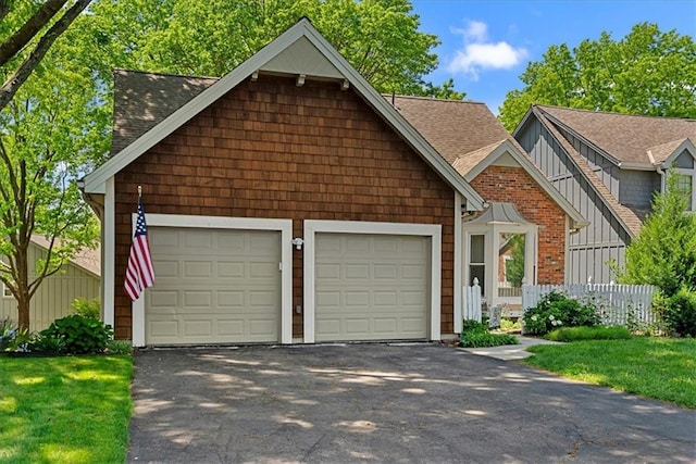 view of front of property featuring an attached garage, driveway, roof with shingles, and fence