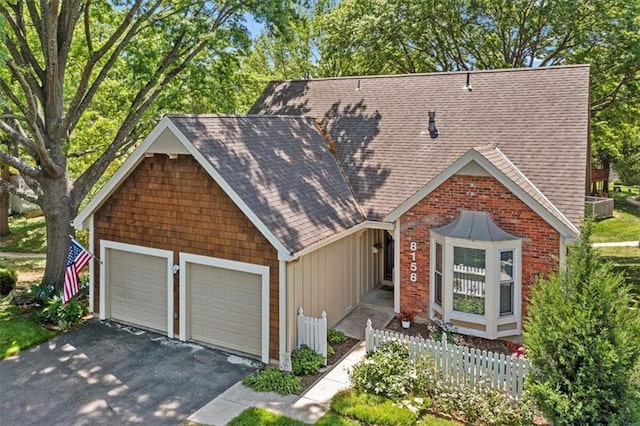view of front of home with roof with shingles, an attached garage, driveway, board and batten siding, and fence