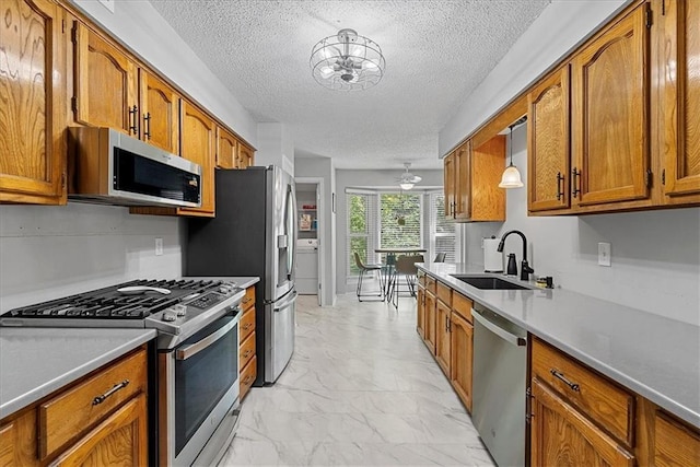 kitchen featuring stainless steel appliances, a sink, brown cabinetry, light marble finish floors, and a textured ceiling