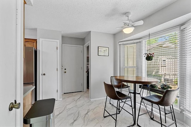 dining room with light marble finish floors, a ceiling fan, a textured ceiling, and baseboards