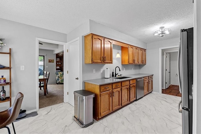 kitchen with a sink, appliances with stainless steel finishes, light countertops, brown cabinetry, and light marble finish flooring