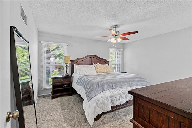 carpeted bedroom featuring multiple windows, a textured ceiling, and a ceiling fan
