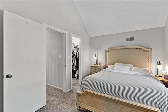 carpeted bedroom with vaulted ceiling, a walk in closet, a closet, and baseboards