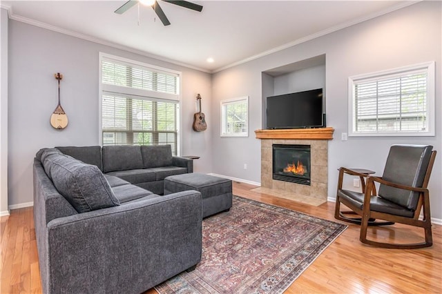 living area featuring a ceiling fan, wood finished floors, ornamental molding, baseboards, and a tile fireplace
