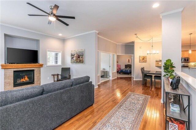 living room with a tiled fireplace, hardwood / wood-style flooring, a ceiling fan, ornamental molding, and a chandelier