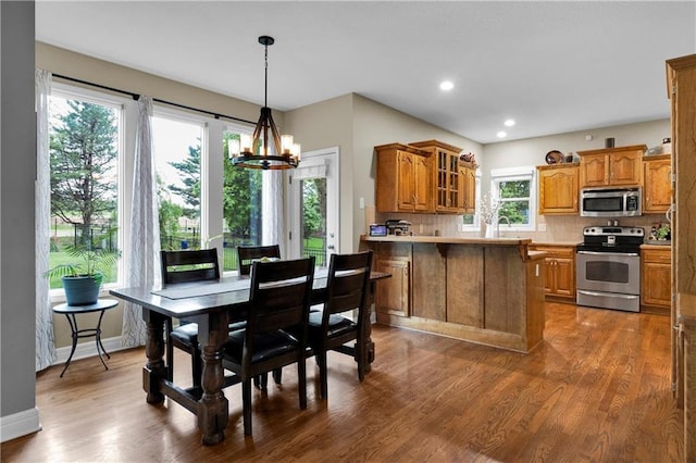 21511 W 100th Ter, Lenexa, KS 66220 - kitchen with appliances with stainless steel finishes, brown cabinets, a peninsula, a chandelier, and glass insert cabinets
