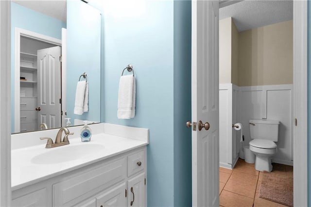 21511 W 100th Ter, Lenexa, KS 66220 - bathroom featuring toilet, vanity, a textured ceiling, tile patterned floors, and a wainscoted wall