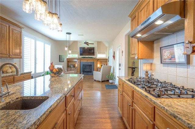2945 W 143rd Ter, Leawood, KS 66224 - kitchen with a sink, under cabinet range hood, black gas stovetop, a fireplace, and backsplash