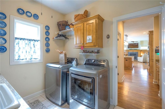 2945 W 143rd Ter, Leawood, KS 66224 - laundry room with separate washer and dryer, a fireplace, cabinet space, light wood-style floors, and baseboards