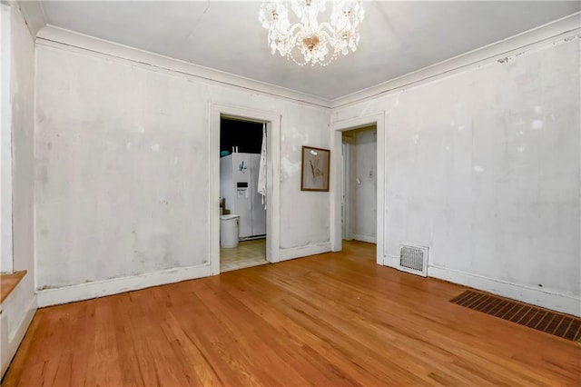 empty room with visible vents, wood finished floors, and a notable chandelier