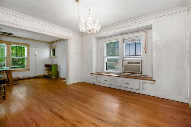 unfurnished dining area with a healthy amount of sunlight, cooling unit, light wood-style flooring, and a chandelier