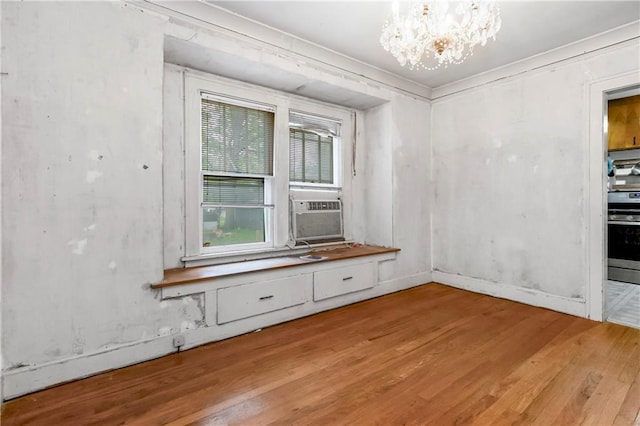 spare room with crown molding, an inviting chandelier, light wood-style floors, baseboards, and cooling unit
