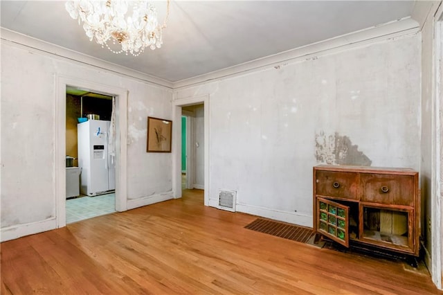 empty room featuring an inviting chandelier, baseboards, wood finished floors, visible vents, and ornamental molding