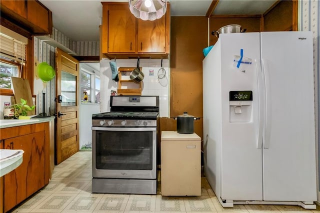 kitchen featuring brown cabinetry, light countertops, stainless steel gas range, light floors, and white fridge with ice dispenser