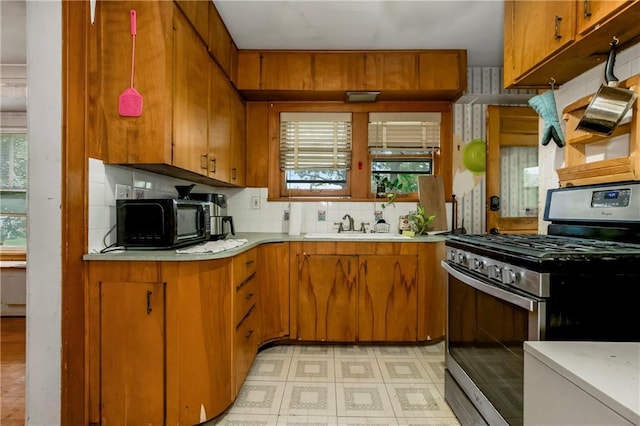 kitchen with decorative backsplash, black microwave, stainless steel range with gas cooktop, light countertops, and a sink