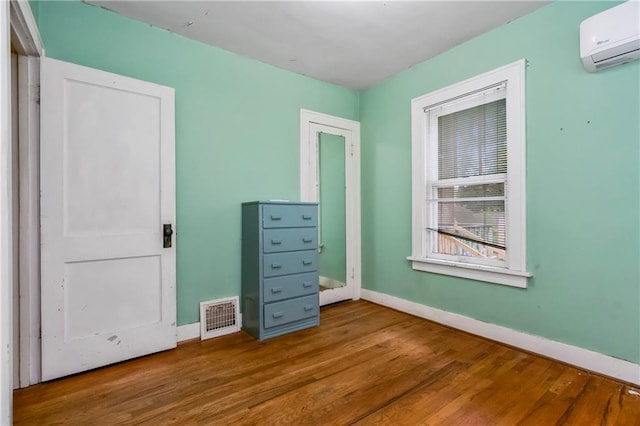 unfurnished bedroom featuring baseboards, an AC wall unit, wood finished floors, and visible vents